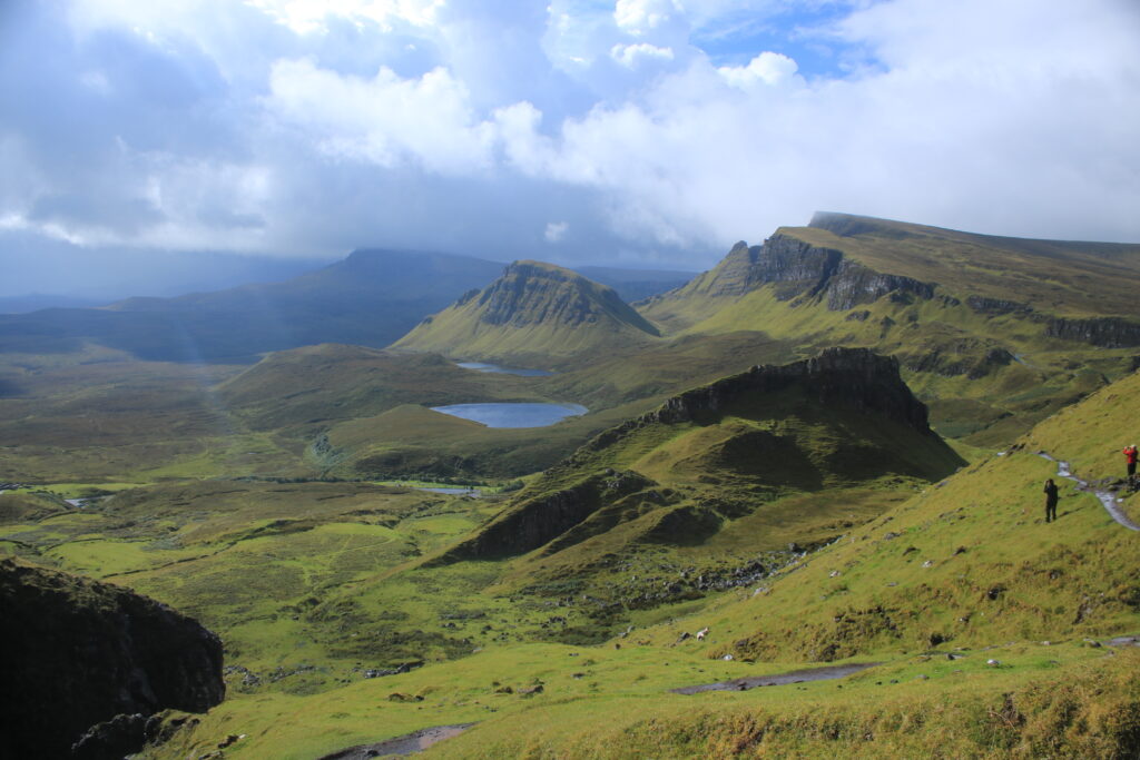 Blick ins Quiraing auf die Haifischflosse. Der Himmel ist mit Wolken bedeckt. Die Sonne scheint etwas. Die Hügel sind mit Gras und Heide bewachsen. 