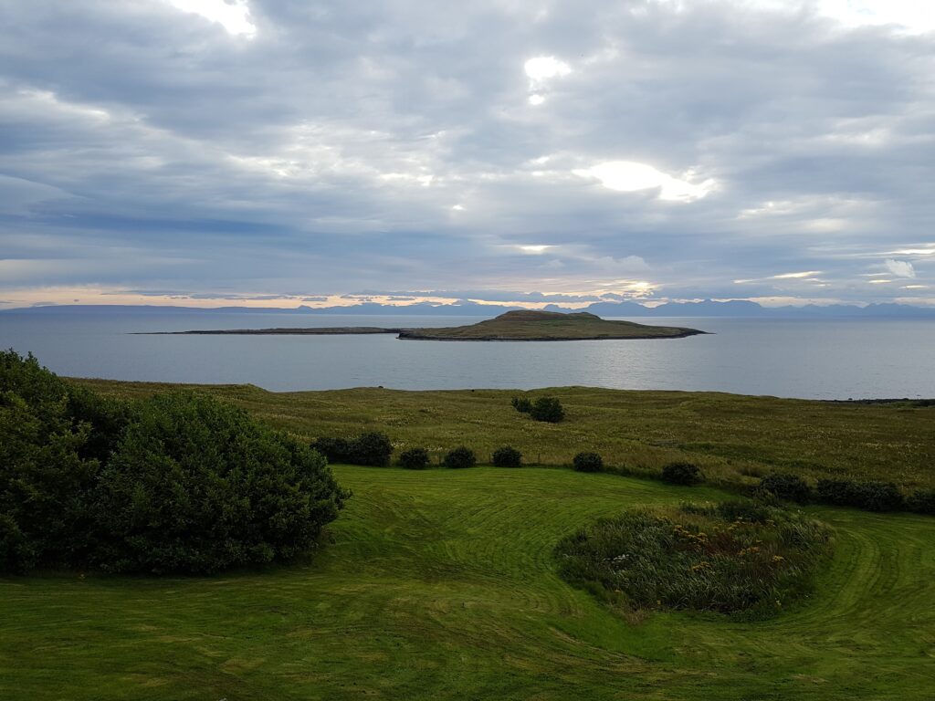 Blick vom Flodigarry Hotel auf The Minch. Im Wasser ist noch eine grasbewachsene Insel zu sehen. Im Vordergrund ist eine gemähte Rasenfläche und einige Büsche