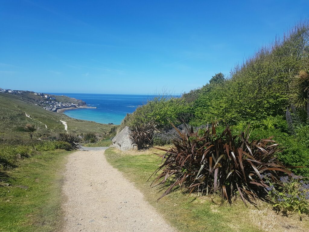 Blick nach Sennen Cove, Cornwall. Das Wasser ist türkis, die Sonne scheint. 