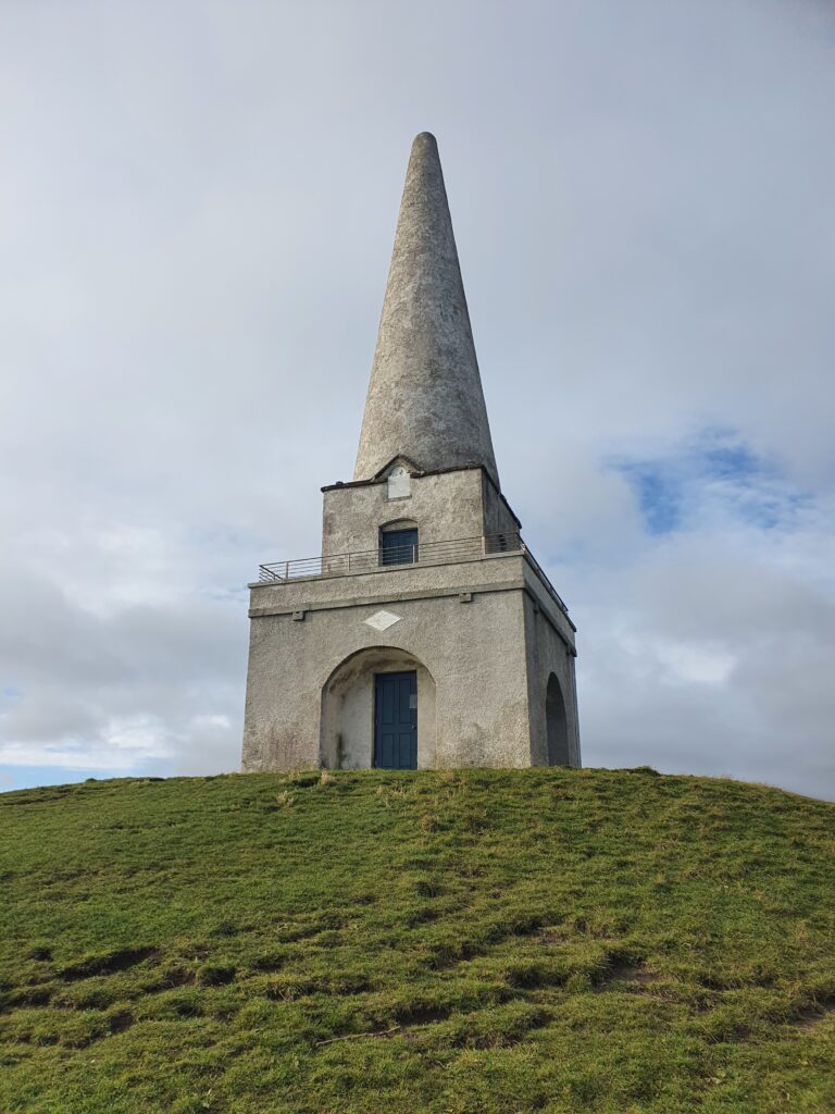 Graues Steindenkmal auf grünem Hügel. 