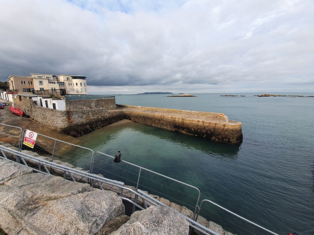 Hafenmauer in Dalkey mit kleinen Steininseln im Wasser.