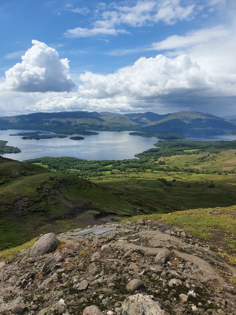 View from Conic Hill over the southern part of Loch Lomond. In the background the foothills of the Arrochar Alps, in the loch the islands of loch Lomond. The sky is blue with white cloudsView over Loch Lomond