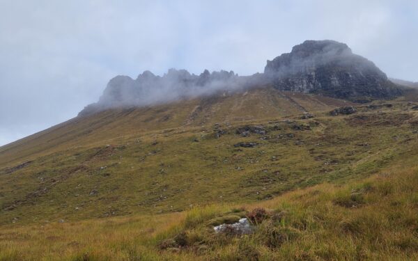 Blick auf die Stac Pollaidh Ridge mit tiefen Wolken. Das Gras ist grün-gelblich